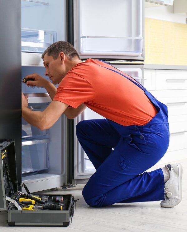 Male-Technician-With-Screwdriver-Repairing-Refrigerator-in-Kitchen Male-Technician-With-Screwdriver-Repairing-Refrigerator-in-Kitchen